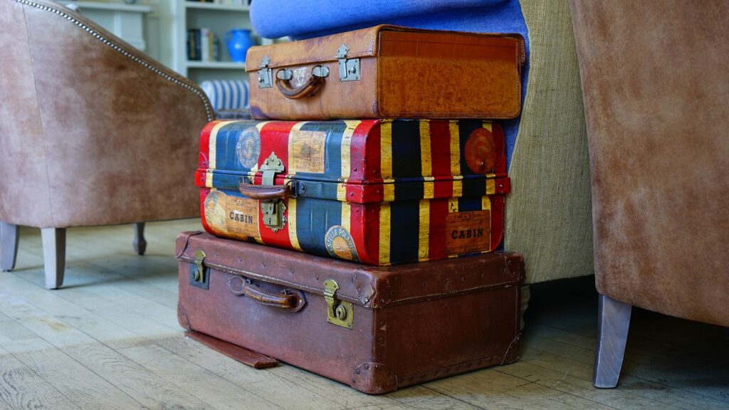 A stack of three suitcases, two of which are brown and one is striped with red, yellow and blue stripes.