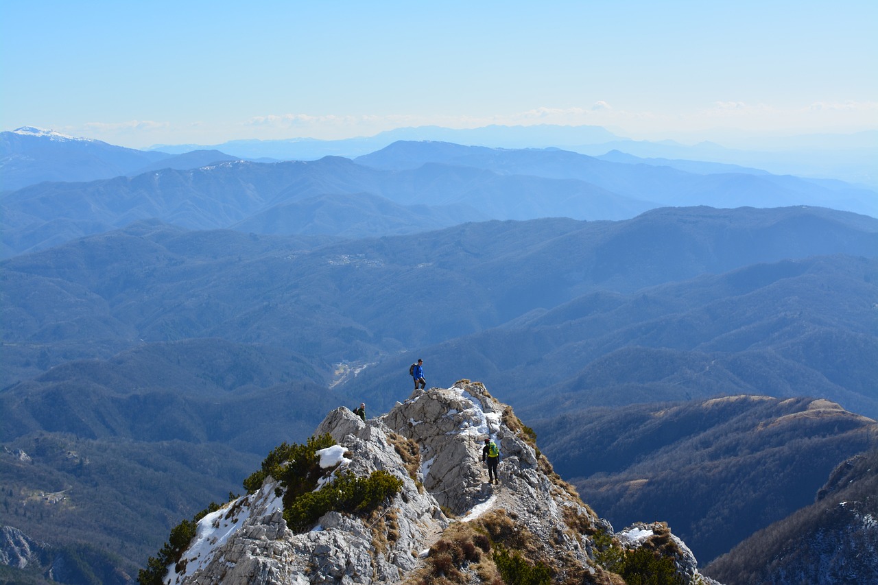 A person on top of a mountain, with hills and mountains in the background on a sunny day