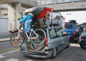 A car, with loads of bags, cases and other items on the roof. The car is clearly weighed down and, how much of all the stuff is actually of any use?