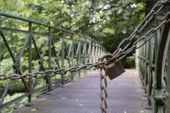 A padlocked chain, blocking the path across a bridge. Life coaching with Gary K. Burns can support you as you overcome the barriers