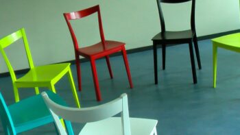 A picture of chairs, all painted in different colours. Sitting around won't help for a better future.