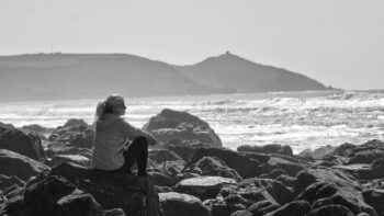 A person sitting on rocks beside the sea, reflecting on life and what comes next.