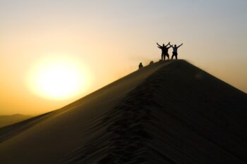 A group of people atop a sand dune, celebrating their journey to the top.