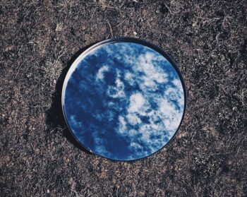 A mirror, resting on barren ground, reflecting the sky above.