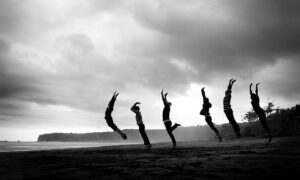 group Gary K Burns A group, jumping for joy, on a beach, with dark skies overhead. They're undeterred, celebrating their success